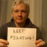 Julian Assange with a poster that reads "keep fighting." Photo: Peoples Dispatch.