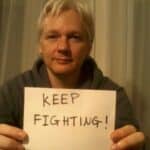 Julian Assange with a poster that reads "keep fighting." Photo: Peoples Dispatch.