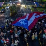 People march along Las Americas Highway as they hold Puerto Rican flags to demand the expulsion of power company Luma amid a continued lack of electricity across the island, in San Juan, Puerto Rico on October 15, 2021. Photo: Ricardo ARDUENGO/AFP via Getty Images.