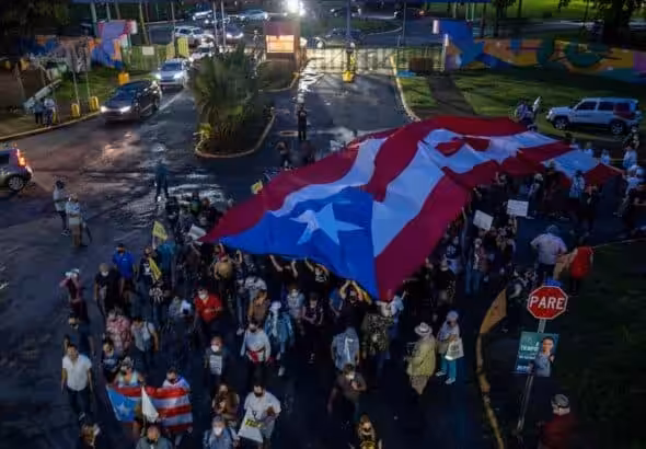 People march along Las Americas Highway as they hold Puerto Rican flags to demand the expulsion of power company Luma amid a continued lack of electricity across the island, in San Juan, Puerto Rico on October 15, 2021. Photo: Ricardo ARDUENGO/AFP via Getty Images.