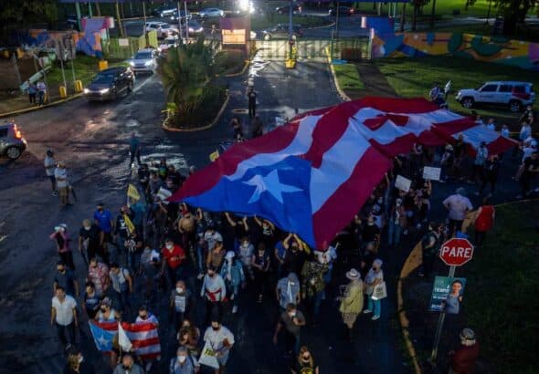 People march along Las Americas Highway as they hold Puerto Rican flags to demand the expulsion of power company Luma amid a continued lack of electricity across the island, in San Juan, Puerto Rico on October 15, 2021. Photo: Ricardo ARDUENGO/AFP via Getty Images.