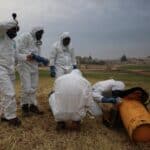 People with biohazard suits making an inspection of a orange object in a field. Photo: OPCW.