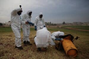 People with biohazard suits making an inspection of a orange object in a field. Photo: OPCW.