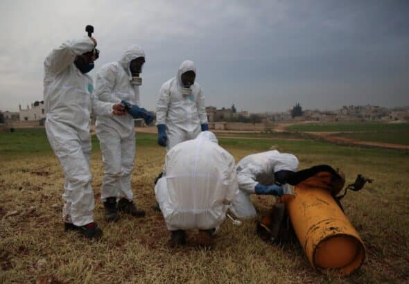 People with biohazard suits making an inspection of a orange object in a field. Photo: OPCW.