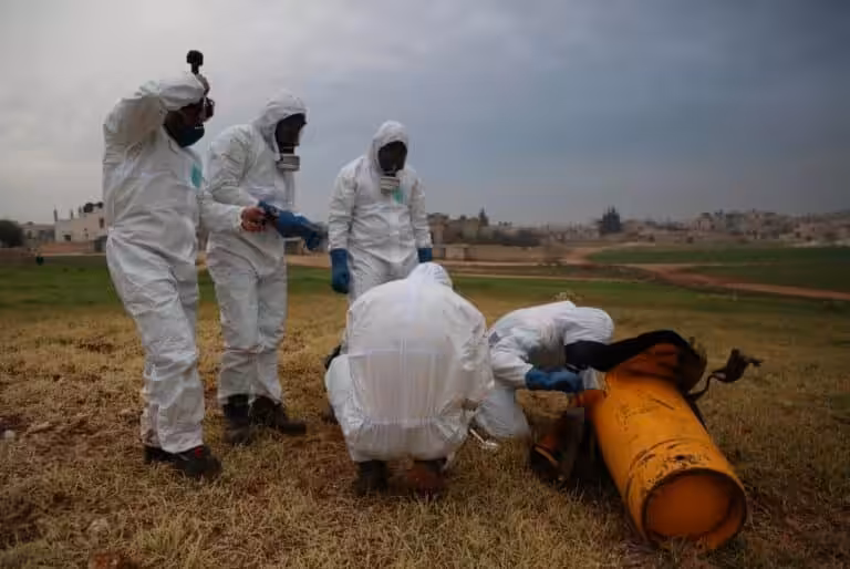 People with biohazard suits making an inspection of a orange object in a field. Photo: OPCW.
