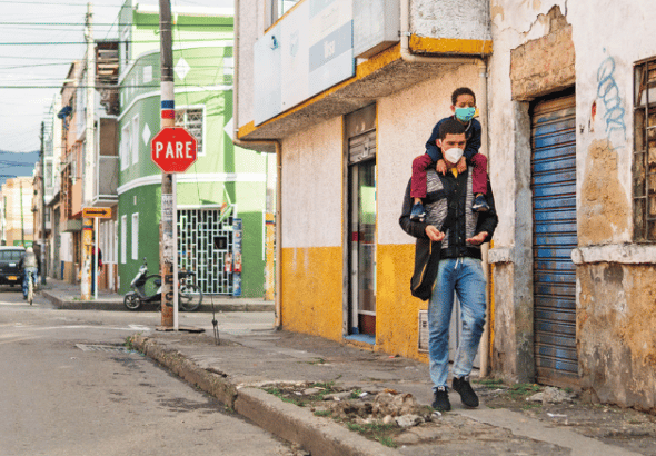 A man walking down a sidewalk in Bogota, Colombia, with a kid climbing on his shoulders. Photo: Alamy.