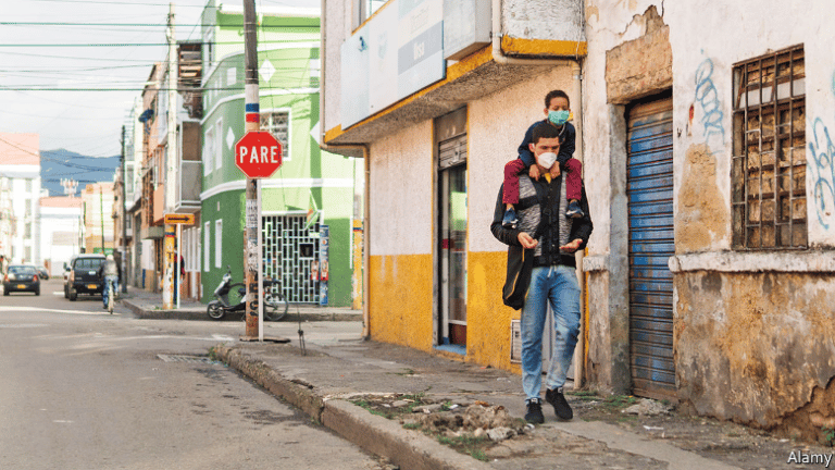 A man walking down a sidewalk in Bogota, Colombia, with a kid climbing on his shoulders. Photo: Alamy.