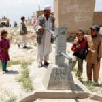 Afghan man surrounded by kids pushing a water pump but no water seen from the other side. A US military truck can be seen in the background. Photo: Kelley J. Stewart via ISAF Headquarters Public Affairs Office from Kabul, Afghanistan – CC BY 2.0.