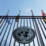 UN emblem on the fence of the United Nations headquarters in New York, with some flags in the background. Photo: United Nations.