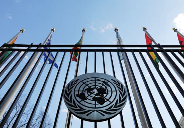 UN emblem on the fence of the United Nations headquarters in New York, with some flags in the background. Photo: United Nations.