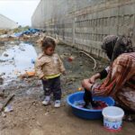 Woman washing cloths on a water bucket using a burka and being watched by a baby girl. In the background a very polluted and dirty area. Photo: xxxxx