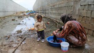 Woman washing cloths on a water bucket using a burka and being watched by a baby girl. In the background a very polluted and dirty area. Photo: xxxxx