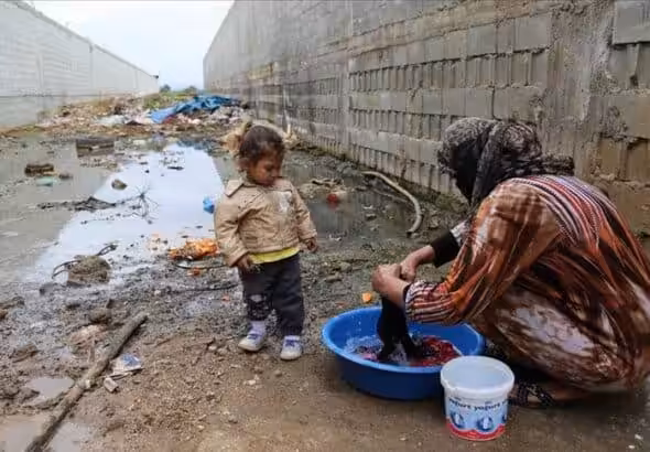 Woman washing cloths on a water bucket using a burka and being watched by a baby girl. In the background a very polluted and dirty area. Photo: xxxxx