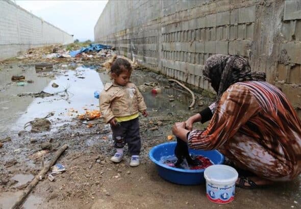 Woman washing cloths on a water bucket using a burka and being watched by a baby girl. In the background a very polluted and dirty area. Photo: xxxxx
