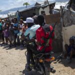 Two armed men ride a motorcycle through the Wharf Jeremy street market in Port-au-Prince, Haiti. Photo: Rodrigo Abd.