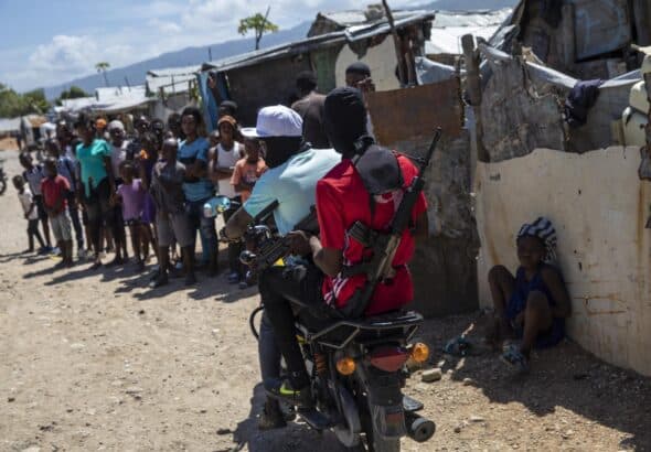 Two armed men ride a motorcycle through the Wharf Jeremy street market in Port-au-Prince, Haiti. Photo: Rodrigo Abd.