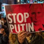 A protestor hanging a banner with the photo of Russian President, Vladimir Putin, and a caption that reads "Stop Putin." Photo: AFP.