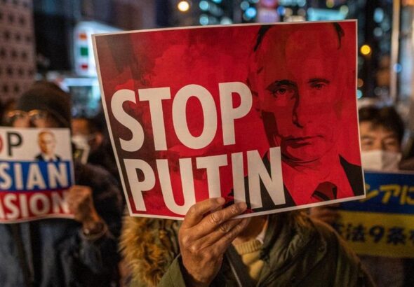 A protestor hanging a banner with the photo of Russian President, Vladimir Putin, and a caption that reads "Stop Putin." Photo: AFP.
