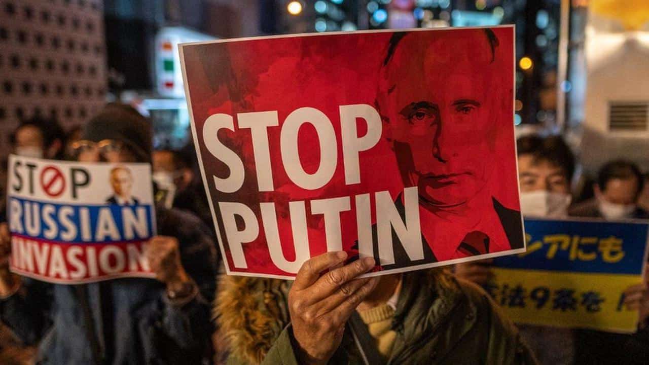 A protestor hanging a banner with the photo of Russian President, Vladimir Putin, and a caption that reads "Stop Putin." Photo: AFP.