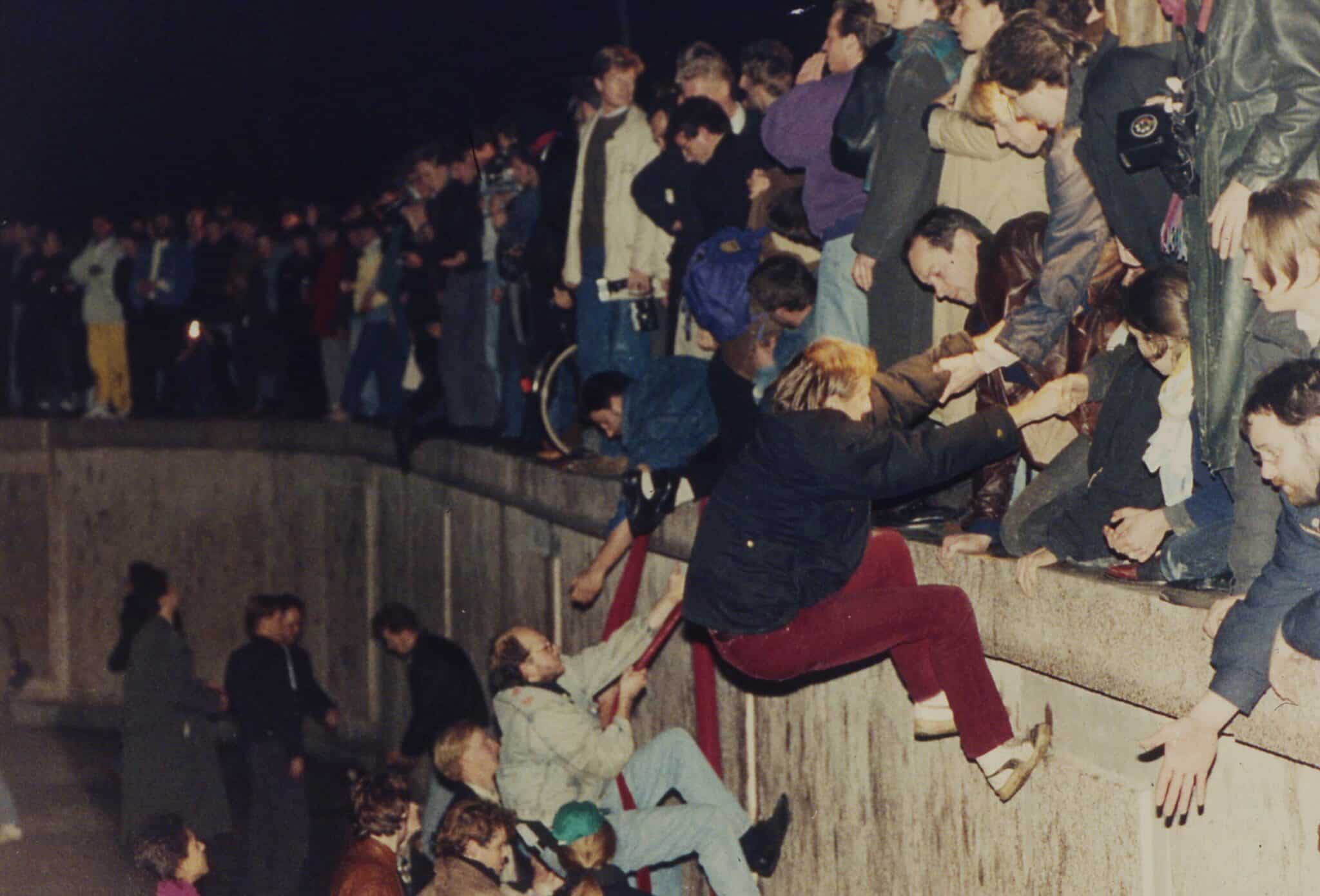 East Berliners climb atop the Berlin Wall with the help of West Berliners in the early morning hours of Nov. 10, 1989. Photo: Jockel Finck AP.