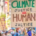 Person in a demonstration holding a banner that reads "Climate Justice equals Human Justice". File photo.