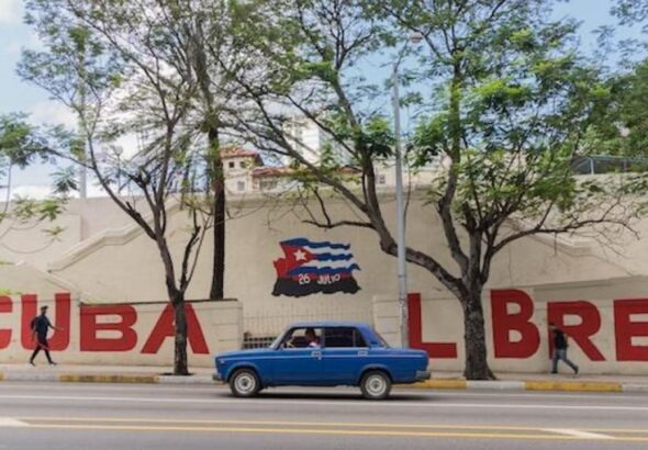A person and a driver passing by a graffiti that says "Cuba Libre". Photo: Yerson Olivares.