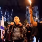 A man wears handcuffs and a mask depicting Israeli prime minister Benjamin Netanyahu, as he takes part in a protest against Netanyahu's new right-wing cabinet and its proposed judicial reforms in Tel Aviv, the occupied territories, on January 14, 2023. Photo: Reuters.