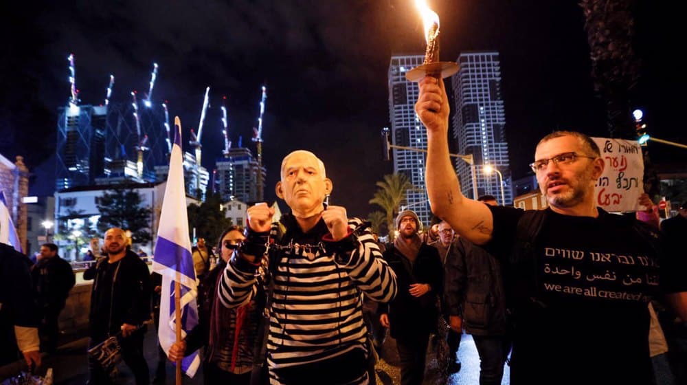 A man wears handcuffs and a mask depicting Israeli prime minister Benjamin Netanyahu, as he takes part in a protest against Netanyahu's new right-wing cabinet and its proposed judicial reforms in Tel Aviv, the occupied territories, on January 14, 2023. Photo: Reuters.