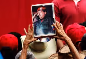 A person holds up a portrait of the late Hugo Chávez, Venezuela's president from 1999 to until his death in 2013, at a March 2019 demonstration. Photo: Ariana Cubillos/Associated Press.