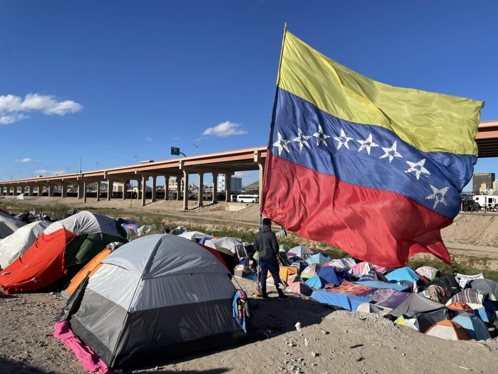 A migrant looks over the Rio Grande river into El Paso, Texas, from under a massive Venezuelan flag at a migrant encampment in Juárez, Mexico, on Thursday, Nov 10, 2022. Photo: Cody Copeland/Courthouse News.