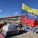 A migrant looks over the Rio Grande river into El Paso, Texas, from under a massive Venezuelan flag at a migrant encampment in Juárez, Mexico, on Thursday, Nov 10, 2022. Photo: Cody Copeland/Courthouse News.