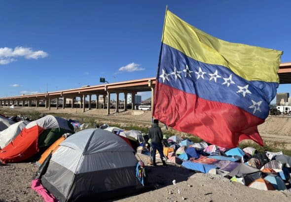 A migrant looks over the Rio Grande river into El Paso, Texas, from under a massive Venezuelan flag at a migrant encampment in Juárez, Mexico, on Thursday, Nov 10, 2022. Photo: Cody Copeland/Courthouse News.