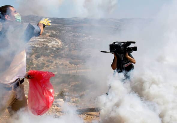 A Palestinian protester, at left, throws a tear gas canister fired by Israeli soldiers away from him as a cameraman records nearby, during a demonstration against Israel's separation barrier in the West Bank village of Bilin, near Ramallah, Friday, Sept. 11, 2009. Israel says the barrier is necessary for security while Palestinians call it a land grab. Photo: Nasser Ishtayeh/Associated Press.