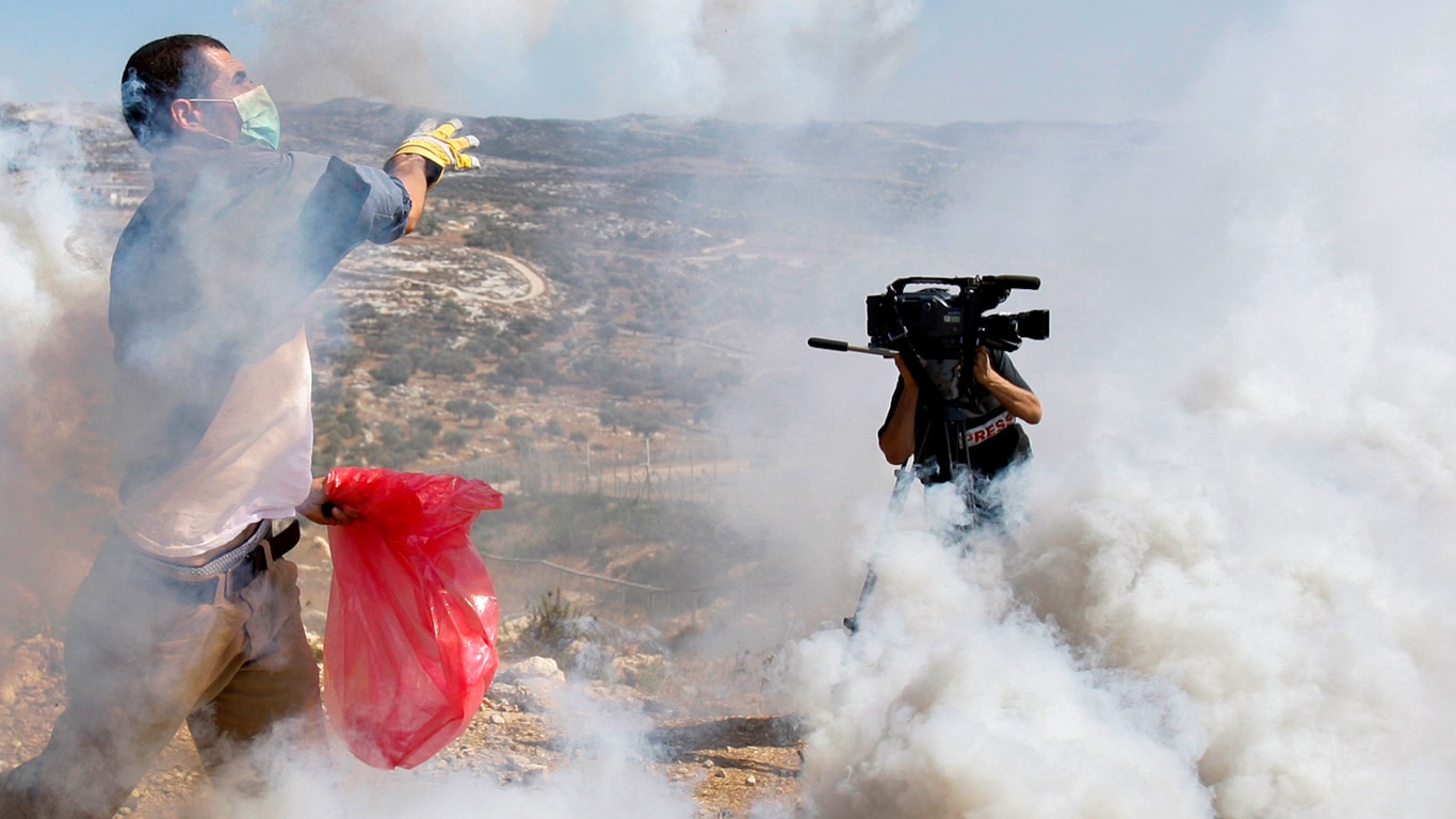 A Palestinian protester, at left, throws a tear gas canister fired by Israeli soldiers away from him as a cameraman records nearby, during a demonstration against Israel's separation barrier in the West Bank village of Bilin, near Ramallah, Friday, Sept. 11, 2009. Israel says the barrier is necessary for security while Palestinians call it a land grab. Photo: Nasser Ishtayeh/Associated Press.