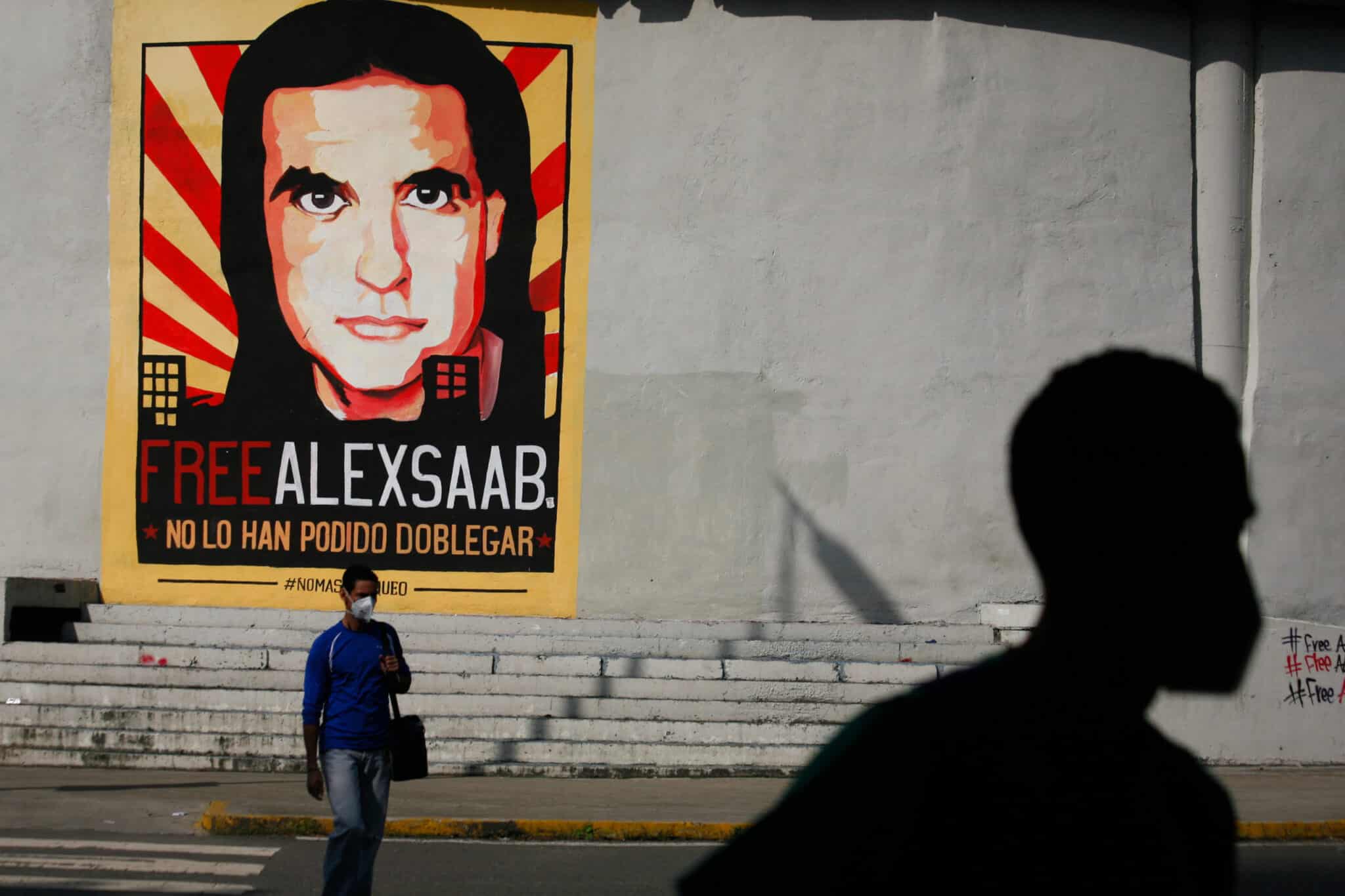 People walk past graffiti in favor of the release of Colombian businessman Alex Saab, amidst the Coronavirus pandemic, on the west side of the city in Caracas, Venezuela on September 8, 2021. Photo: Javier Campos/NurPhoto via Getty Images.