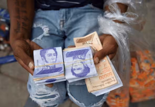A seller holds bolívar notes and plastic bags with products. Photo: AP.