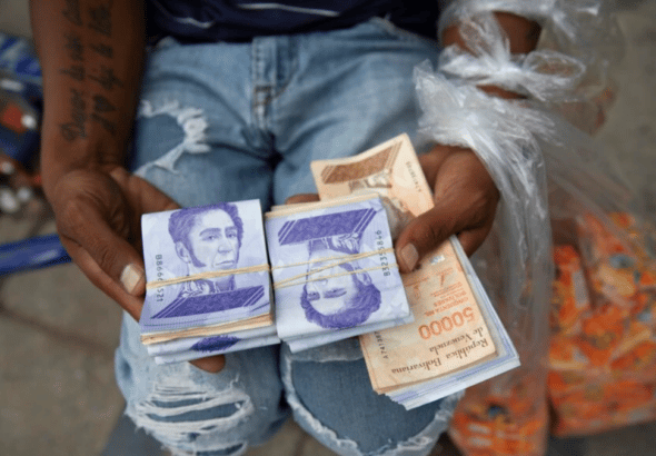 A seller holds bolívar notes and plastic bags with products. Photo: AP.