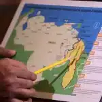 A person's hands use a pencil to point to a Venezuelan map that depicts the Essequibo territory in yellow surrounded by multiple border lines drawn by the UK, next to a timeline of the territorial dispute. Photo: File photo.