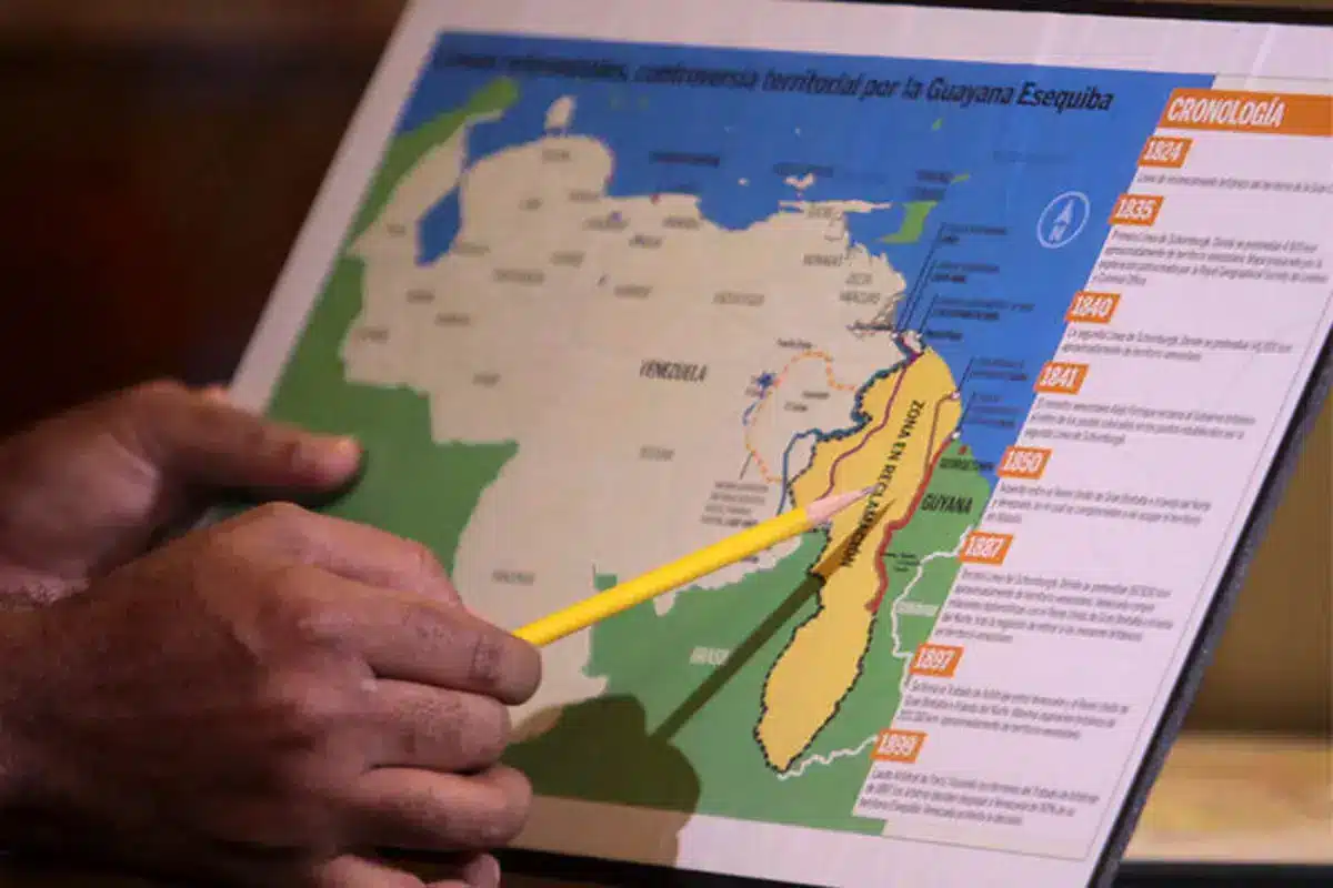 A person's hands use a pencil to point to a Venezuelan map that depicts the Essequibo territory in yellow surrounded by multiple border lines drawn by the UK, next to a timeline of the territorial dispute. Photo: File photo.