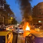 A motorcycle belonging to security forces burns in a street crowded with cars amidst 2022 riots in Tehran, Iran. Photo: West Asia News Agency.