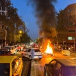 A motorcycle belonging to security forces burns in a street crowded with cars amidst 2022 riots in Tehran, Iran. Photo: West Asia News Agency.