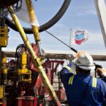 An oil worker maneuvering an oil rig, with a Chevron flag flying in the background. File photo.