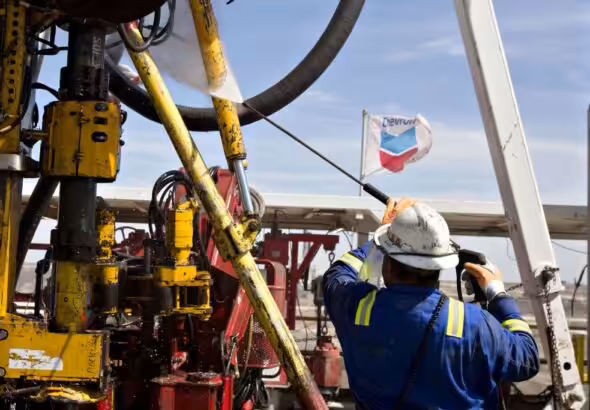 A worker maneuvering an oil rig with a Chevron flag flying in the background. Photo: File photo.