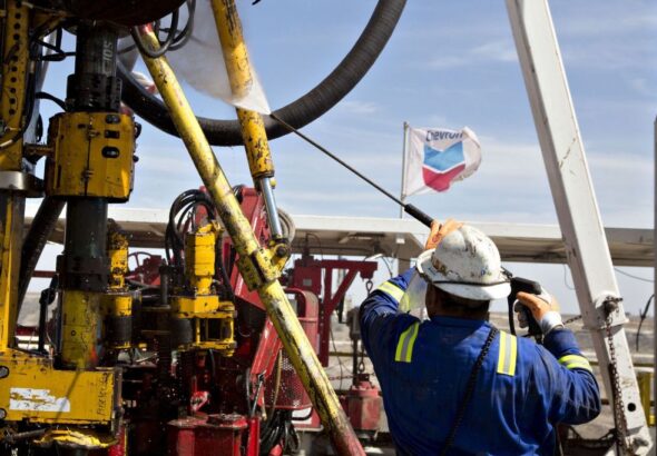 An oil worker maneuvering an oil rig, with a Chevron flag flying in the background. File photo.