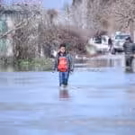 Young person wading through recent flooding in northern Syria. Photo: Getty Images.