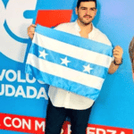 Advertisement of the Revolución Ciudadana party where a person holds a flag and in a strip at the bottom it reads : "return with more strength" and on the right side can be seen former president Rafael Correa smiling. File photo.