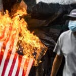 San Salvador, El Salvador.- 2021/07/30: A demonstrator runs as the United States flag goes up in flames, symbolizing US backed militarism during the massacre of students in 1975. Photo: Camilo Freedman/SOPA Images/LightRocket via Getty Images.