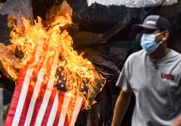 San Salvador, El Salvador.- 2021/07/30: A demonstrator runs as the United States flag goes up in flames, symbolizing US backed militarism during the massacre of students in 1975. Photo: Camilo Freedman/SOPA Images/LightRocket via Getty Images.