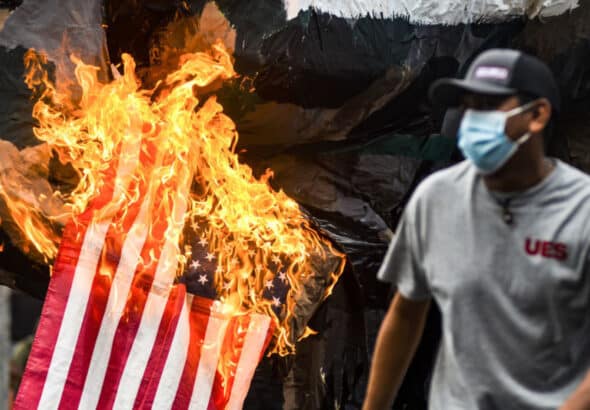 San Salvador, El Salvador.- 2021/07/30: A demonstrator runs as the United States flag goes up in flames, symbolizing US backed militarism during the massacre of students in 1975. Photo: Camilo Freedman/SOPA Images/LightRocket via Getty Images.