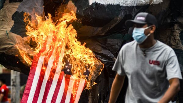 San Salvador, El Salvador.- 2021/07/30: A demonstrator runs as the United States flag goes up in flames, symbolizing US backed militarism during the massacre of students in 1975. Photo: Camilo Freedman/SOPA Images/LightRocket via Getty Images.